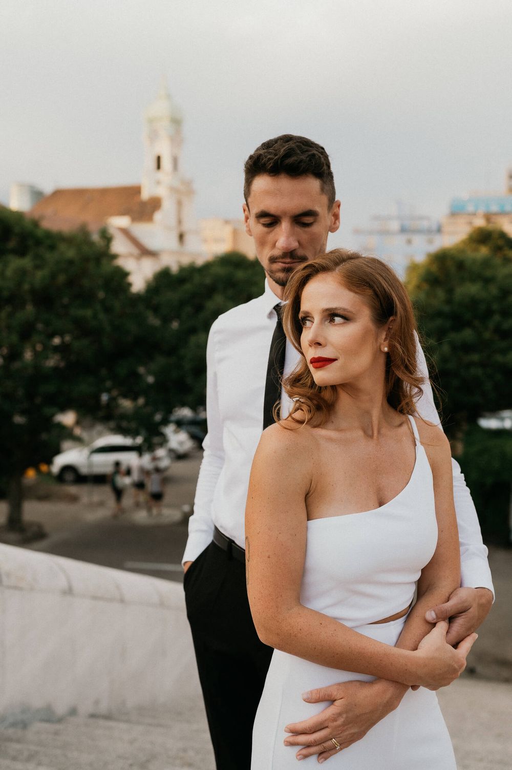 Romantic rooftop portrait with church spire and cityscape in background.