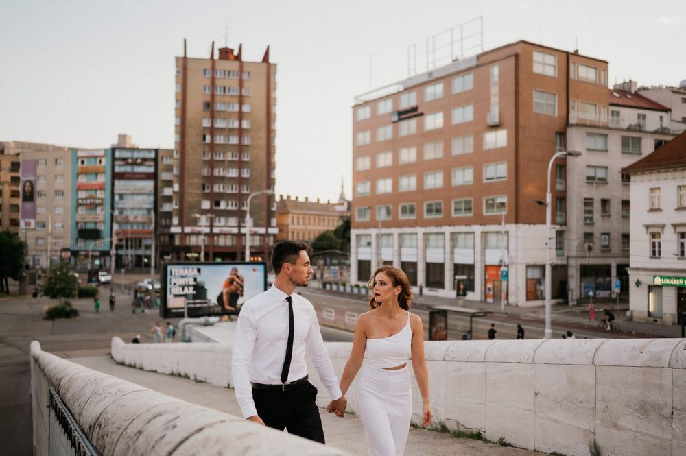 Couple in wedding attire posing on urban concrete ledge with apartments in background.