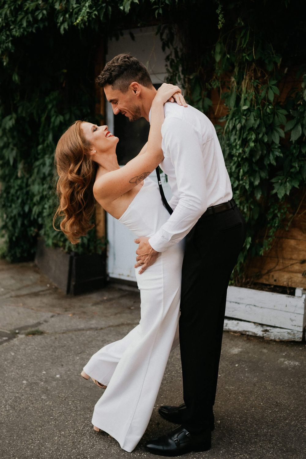 A romantic couple in formal attire share an intimate dance pose against a leafy green backdrop.
