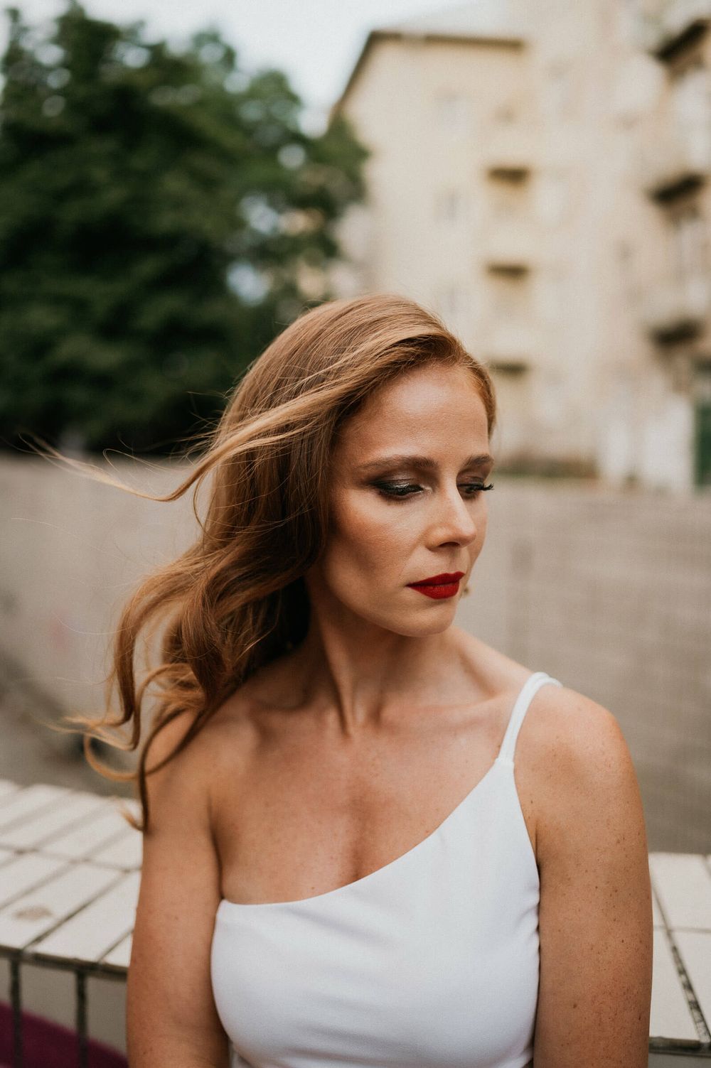 A portrait of someone in a white one-shoulder dress with flowing hair and elegant makeup.