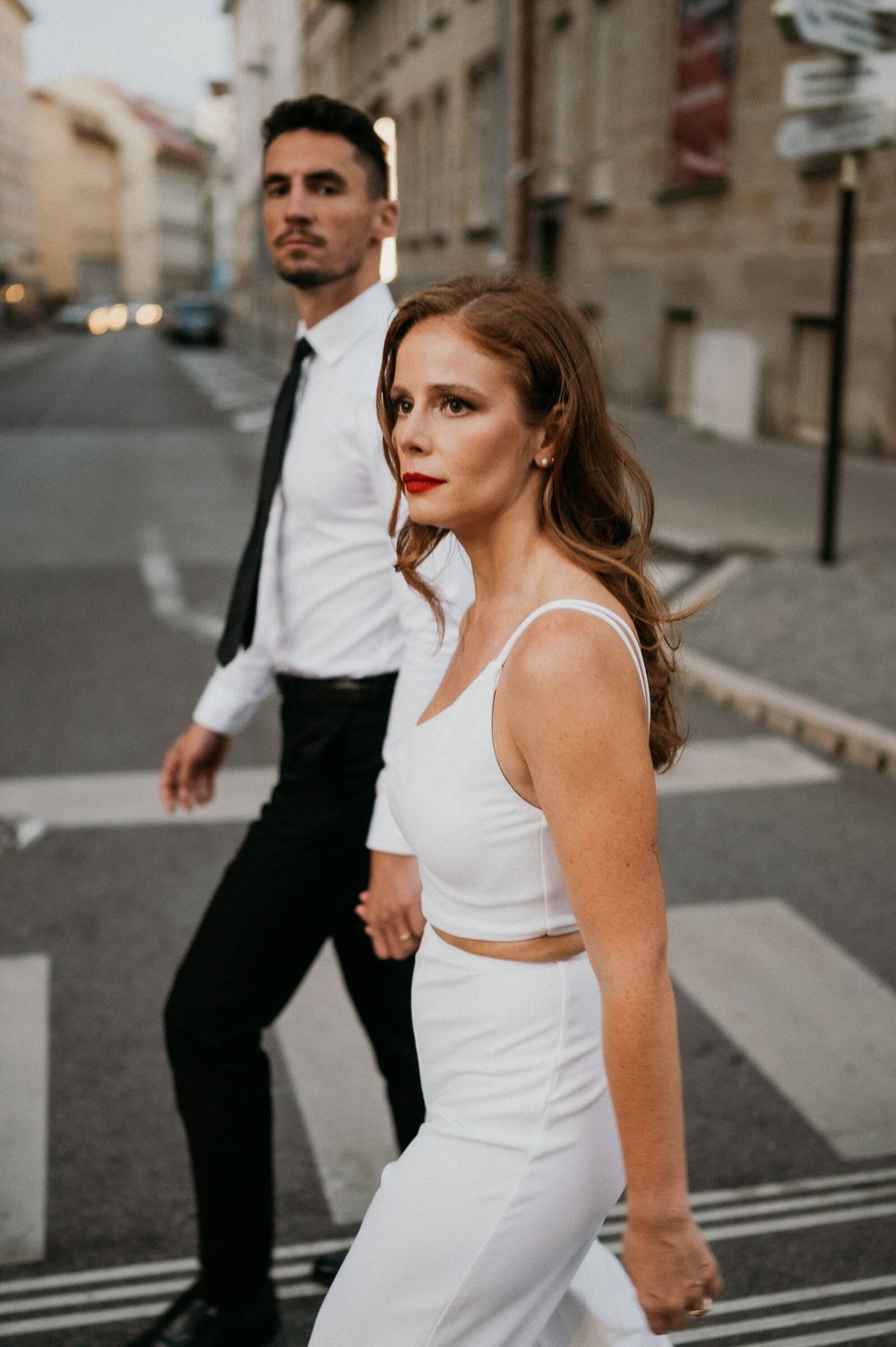 A couple in contrasting black and white outfits walking through city streets at dusk.