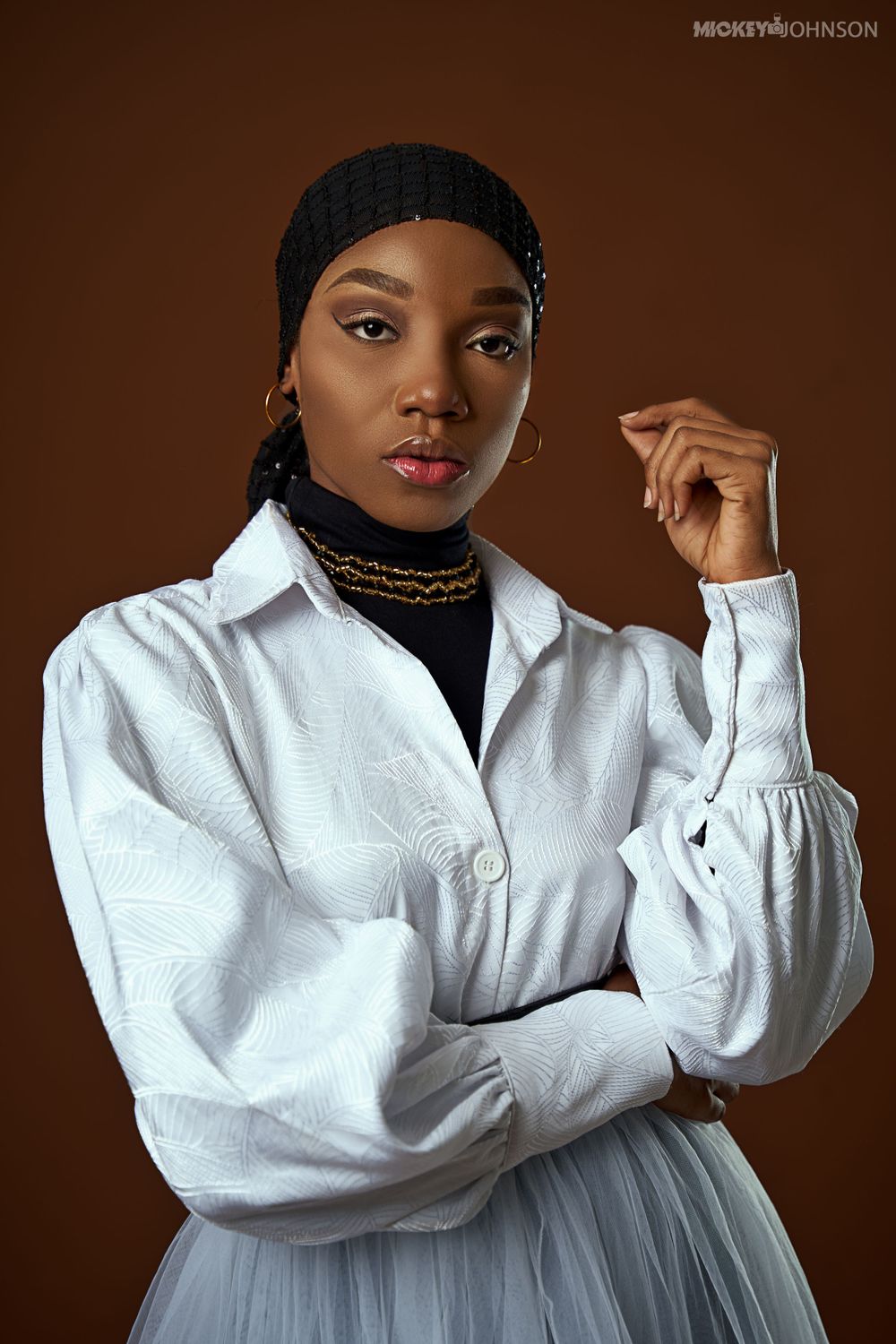 Classic white button-down shirt styled with headscarf against warm brown background.