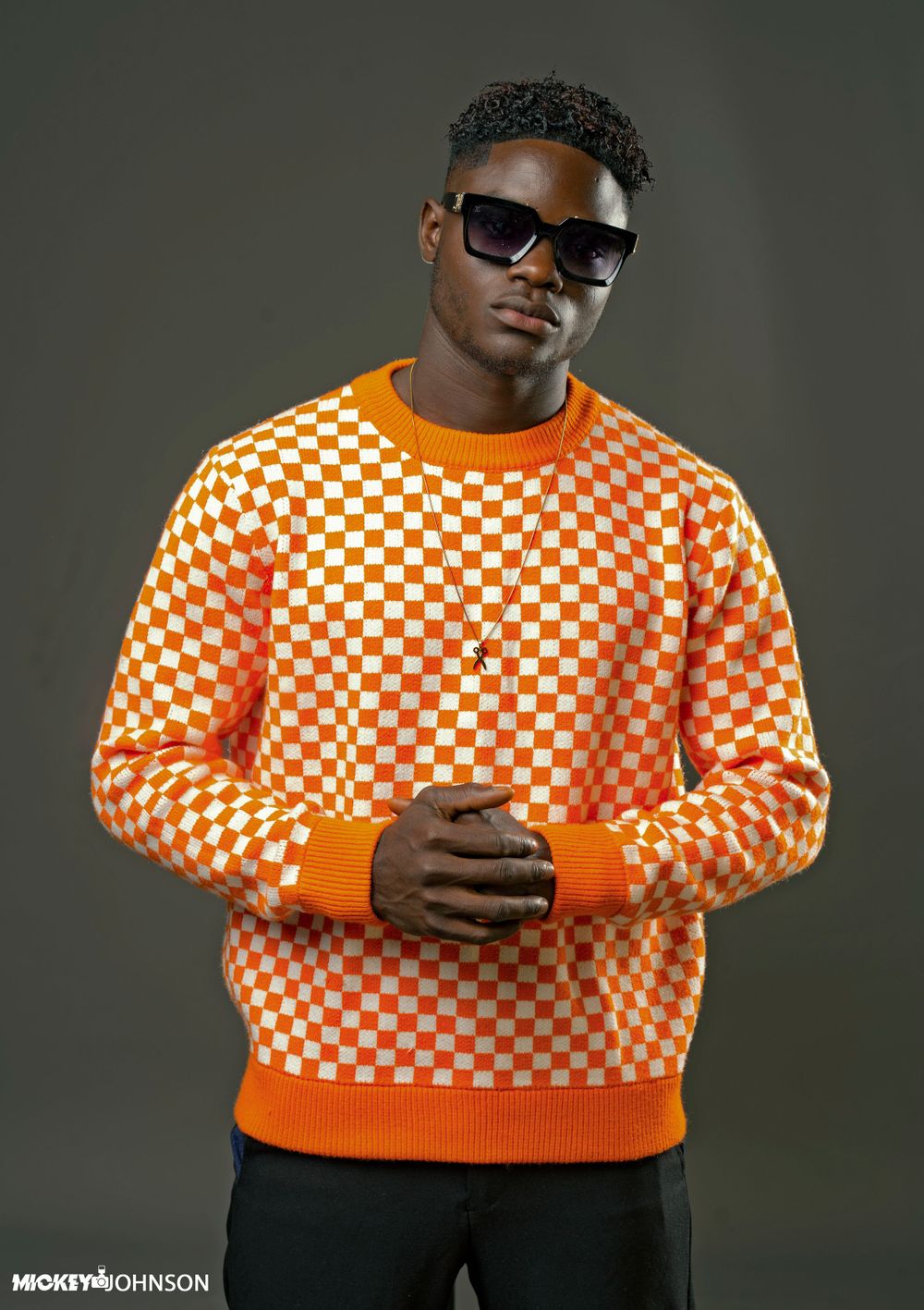 Person wearing orange and white checkered sweater in studio photoshoot.
