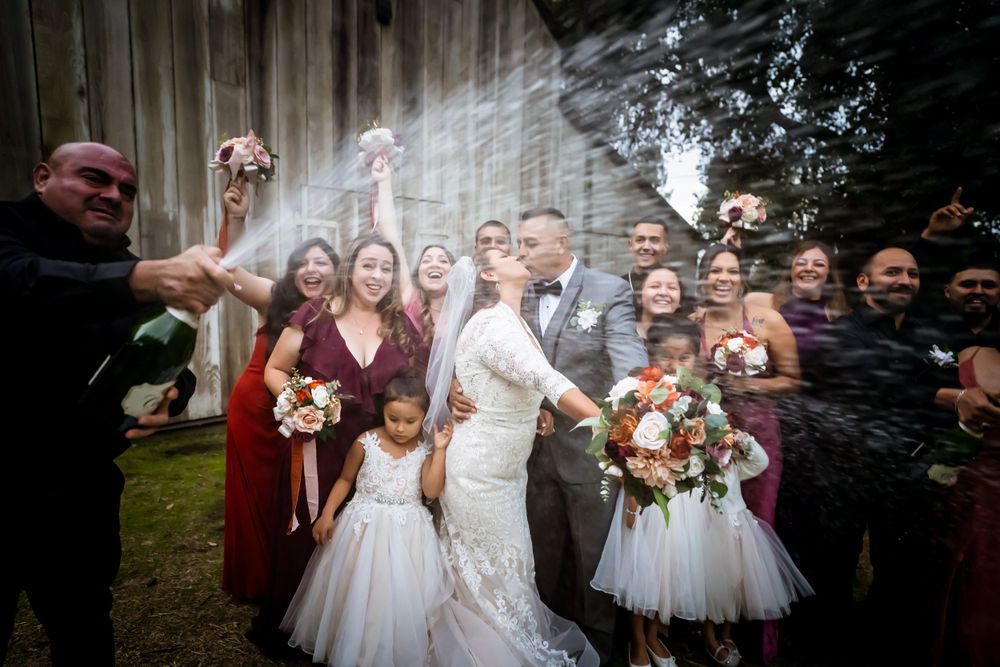 A joyful wedding celebration with guests popping champagne outdoors surrounded by flower decorations.