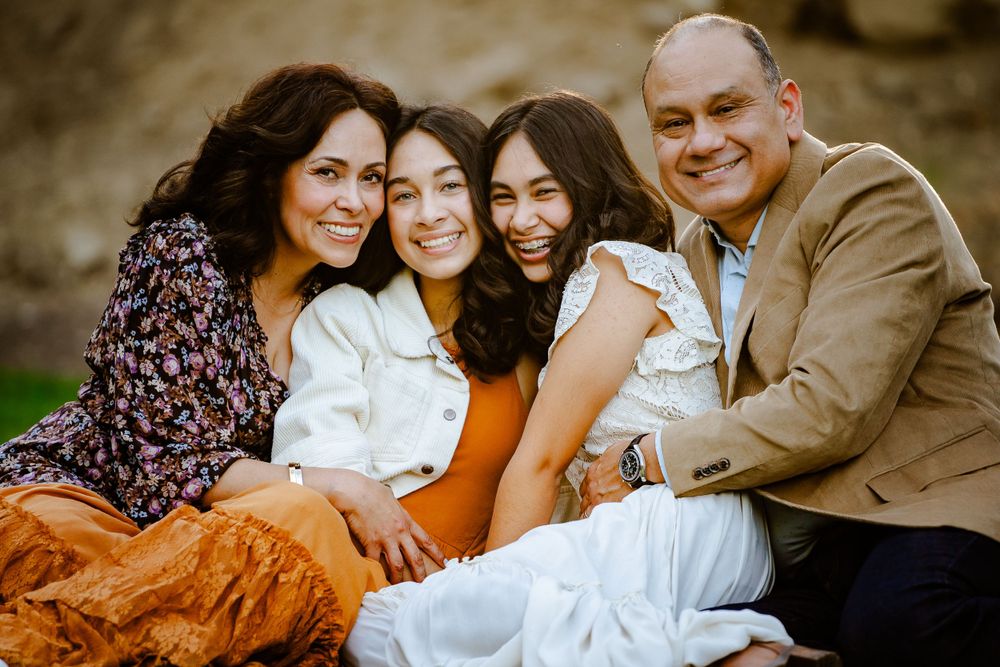 A casual outdoor family portrait featuring four people sitting together in coordinated earth-tone outfits.