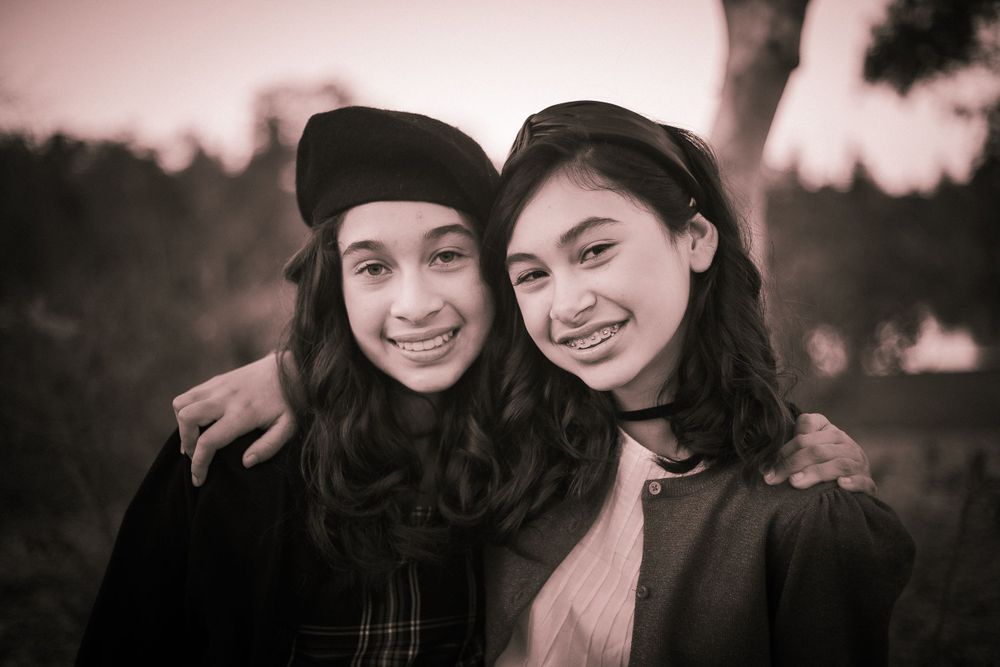 A warm toned portrait of two friends embracing and smiling outdoors at sunset.