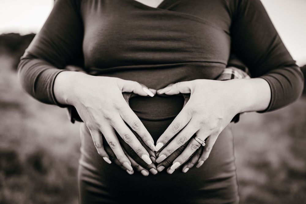 Black and white photo of hands forming a heart shape over a pregnant belly.