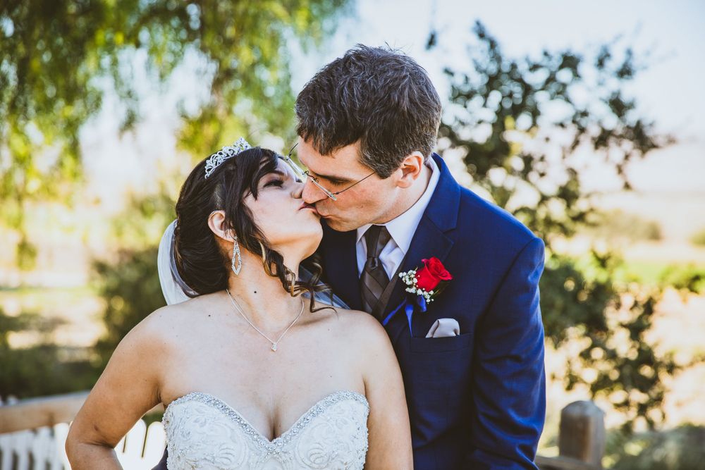 Romantic wedding couple sharing a tender kiss outdoors with natural light filtering through trees.
