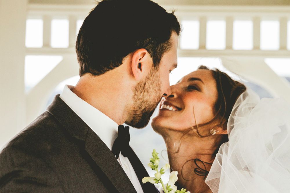 Intimate moment between newlyweds sharing a kiss under bride's delicate veil.