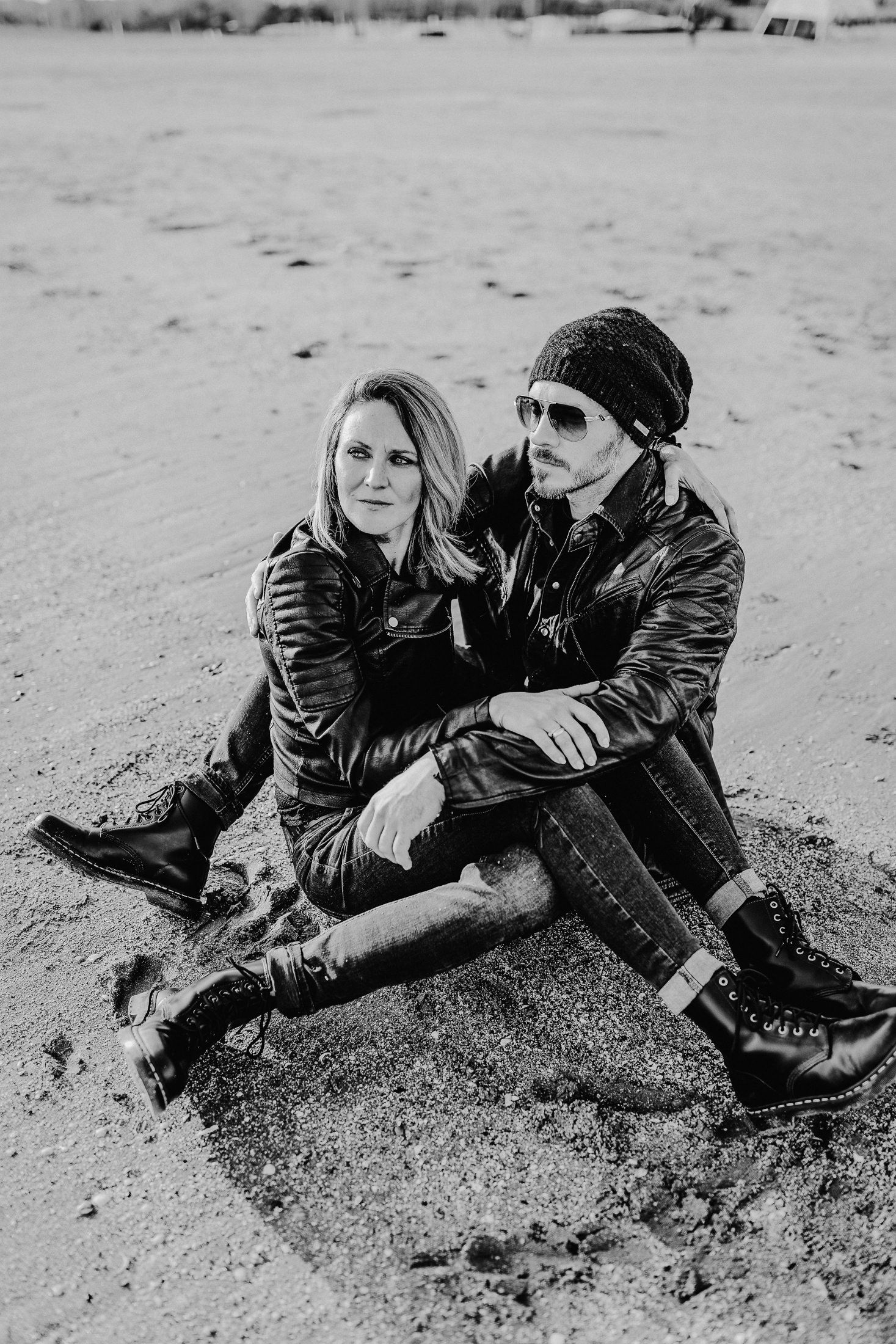 Künstlerisches Schwarz-Weiß-Foto eines Paares, das zusammen am Strand in lässiger Winterkleidung sitzt.
