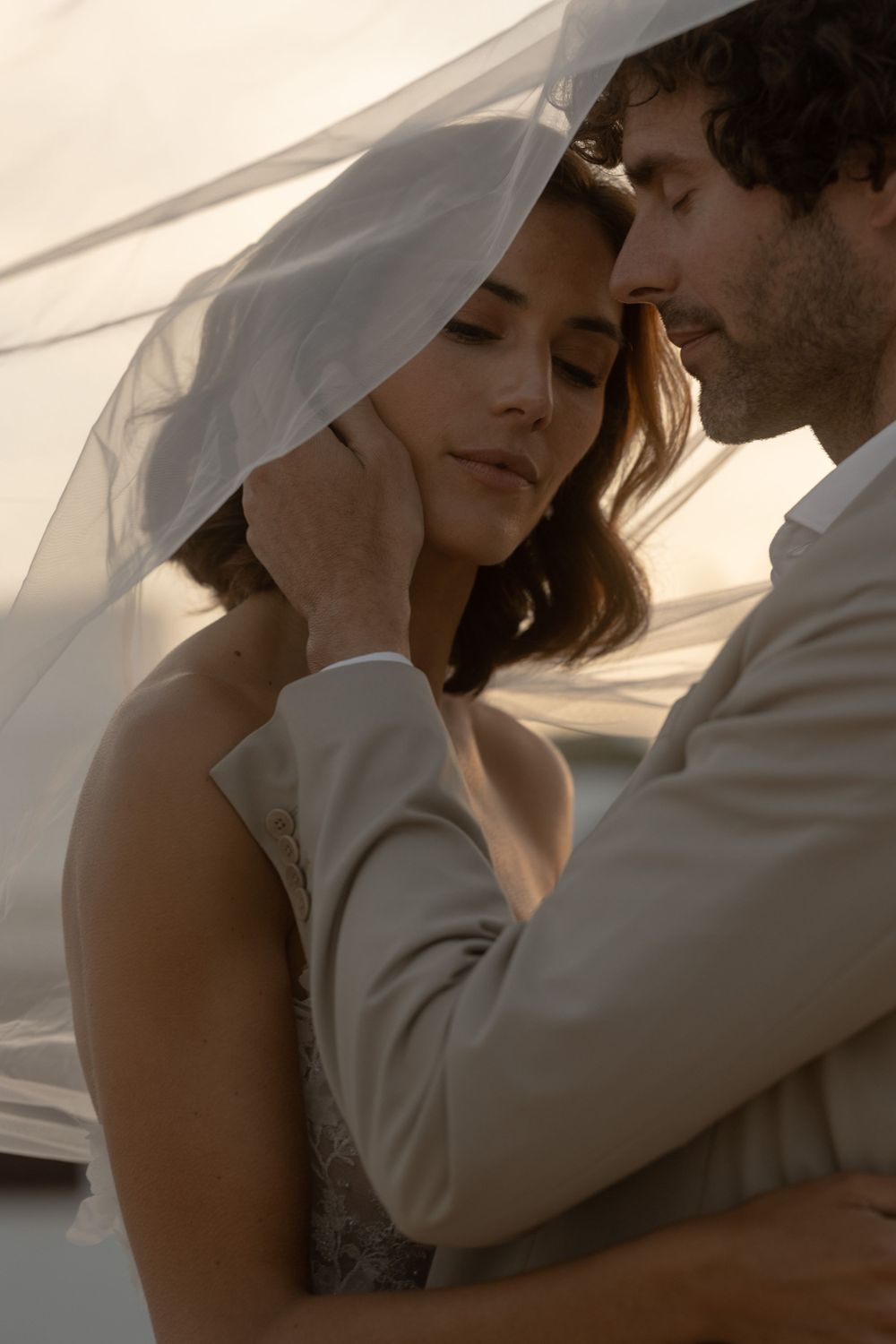 An intimate wedding moment captured through a delicate veil at sunset.