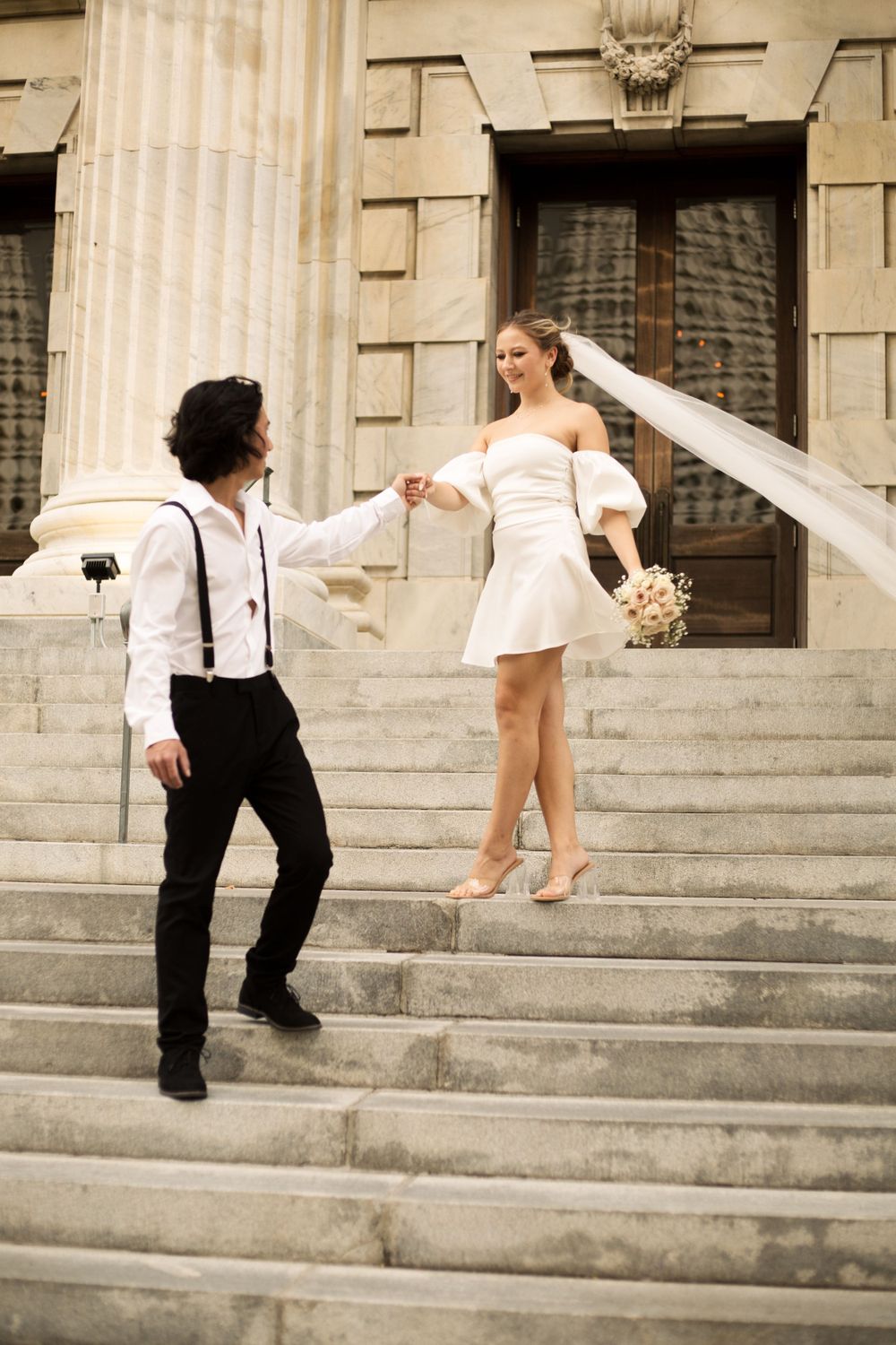 Couple dancing on ornate building steps with white dress and suspenders.
