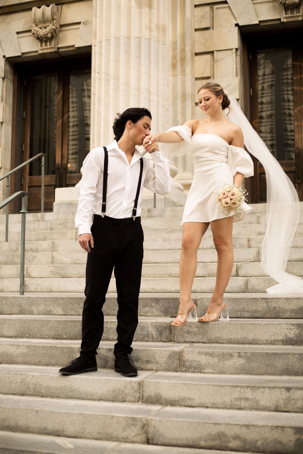 Couple shares intimate moment on historic building steps with flowing veil and bouquet.