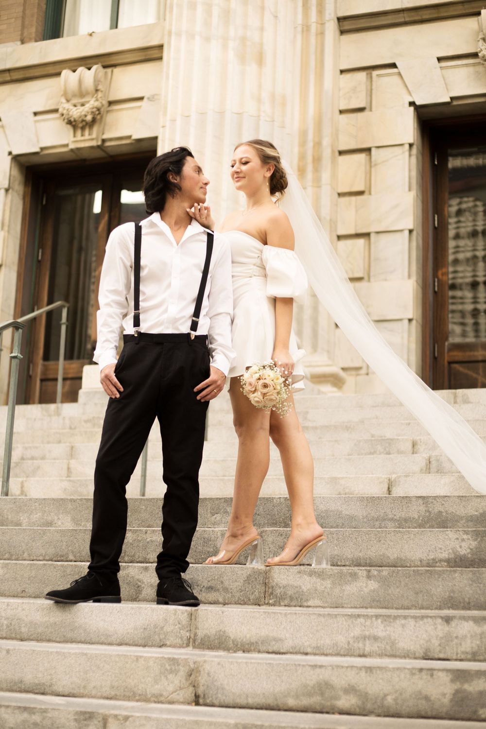 Joyful wedding couple laughing together on grand stone steps with classical architecture.