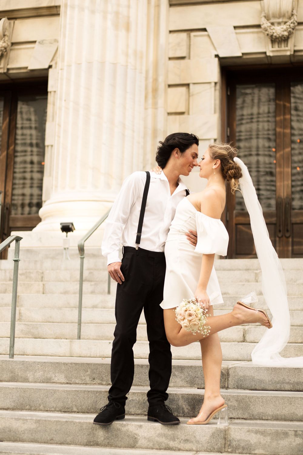 Romantic wedding moment captured on elegant stone steps with classical columns.