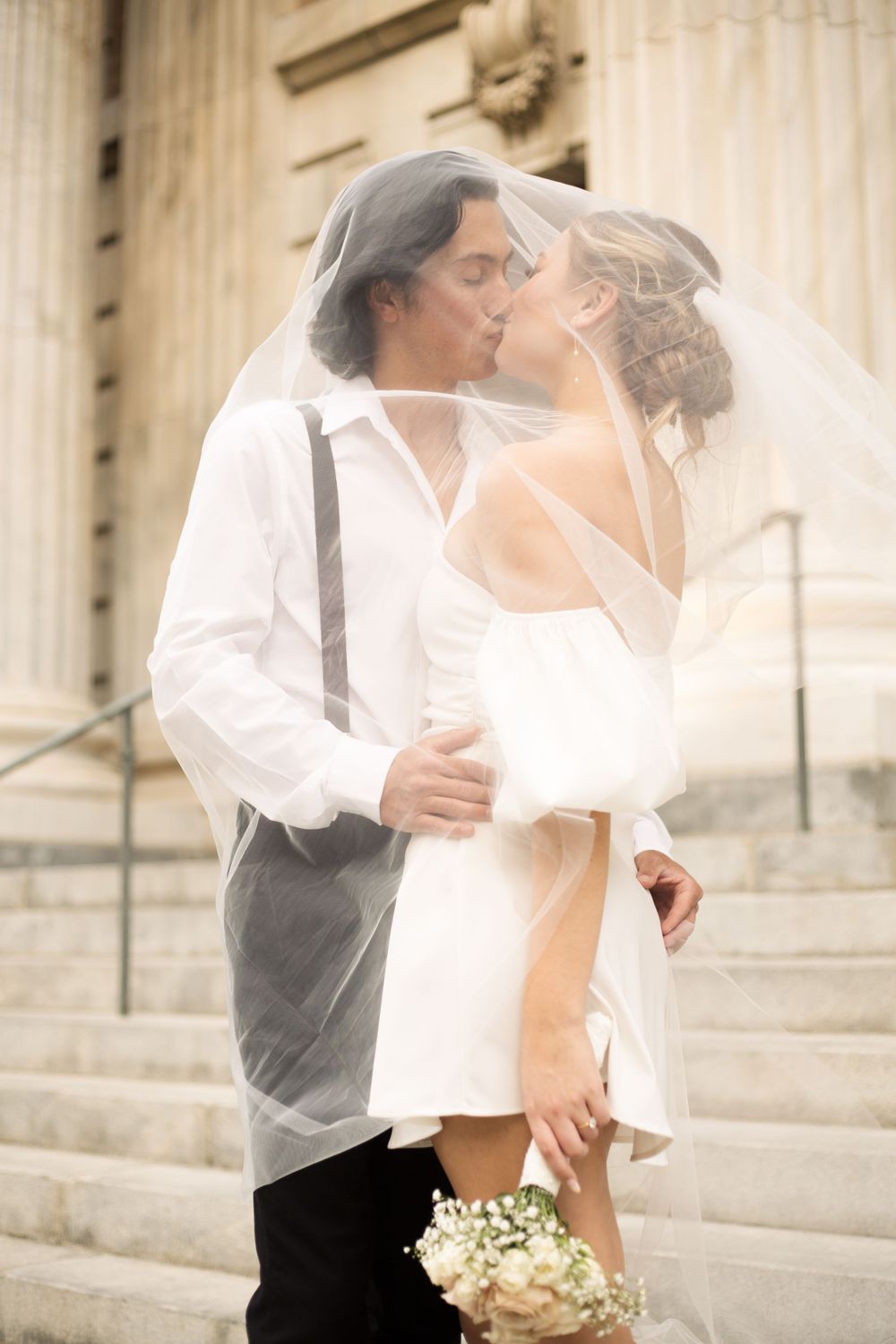 Intimate wedding moment under flowing veil on classical building steps.