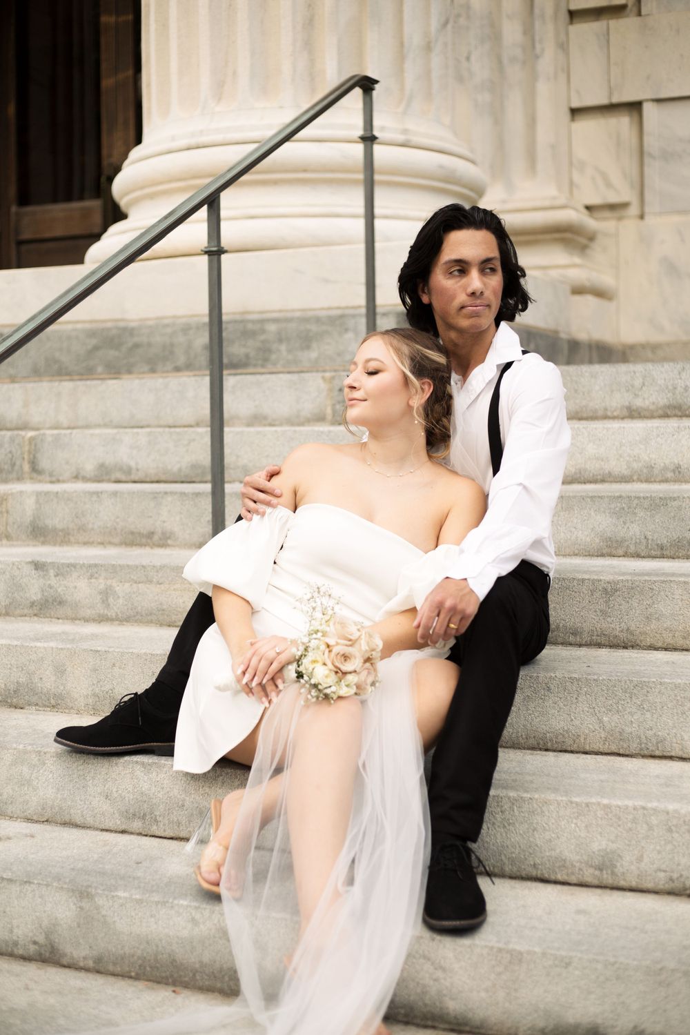 Couple in romantic pose on elegant stone steps with classical architecture.