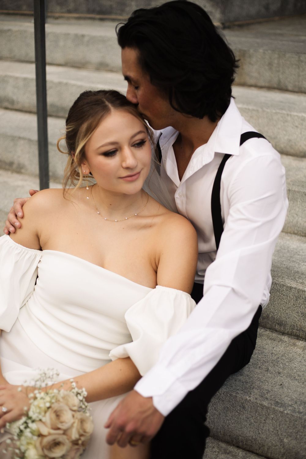 A romantic wedding photo of a couple in white and black attire embracing on stone steps.