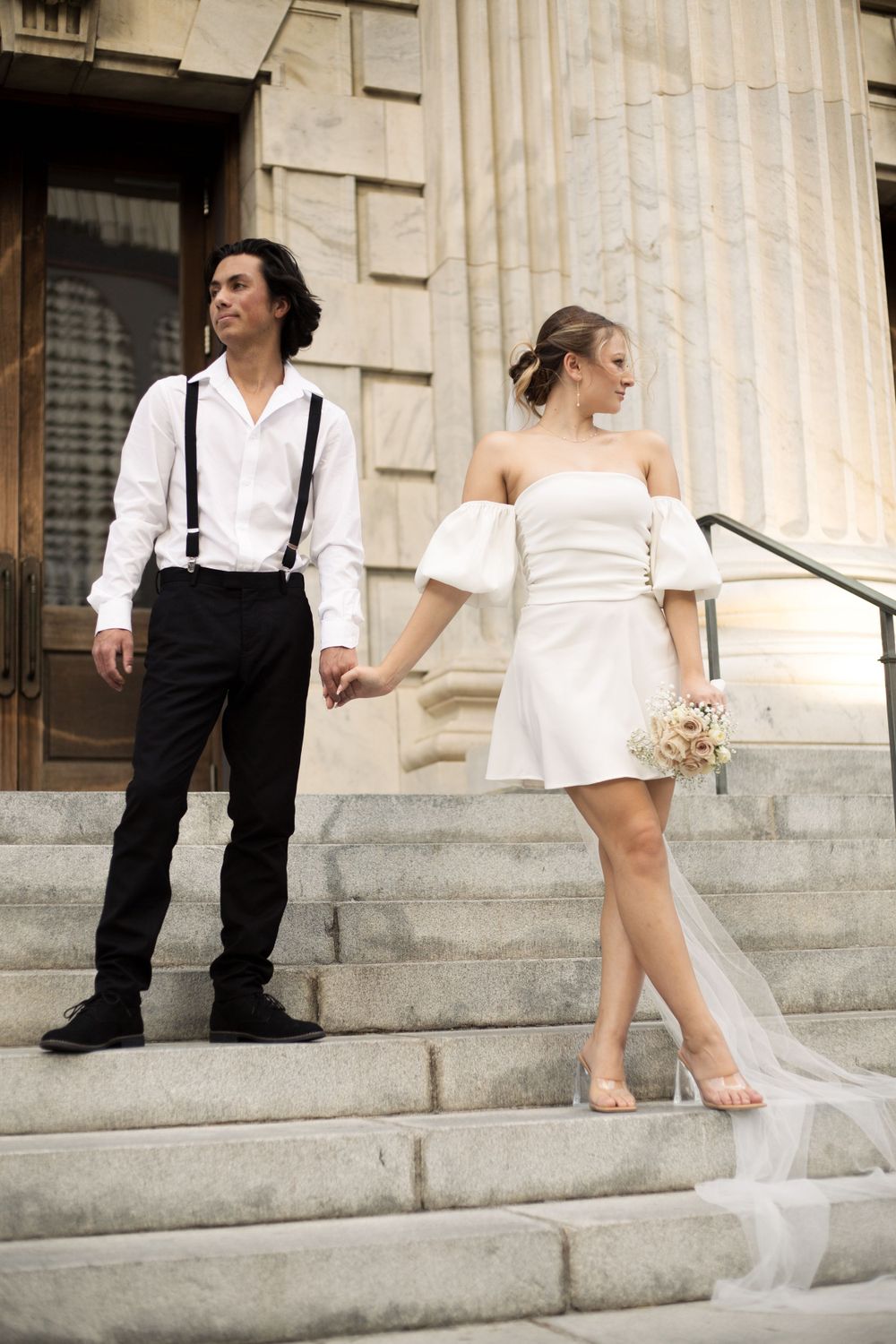 A stylish couple in wedding attire posing casually on classic stone steps with columns.
