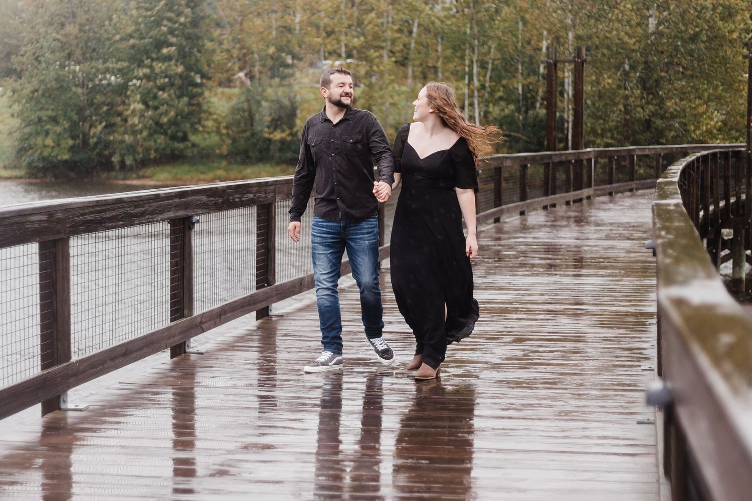 A couple walks along a wet wooden boardwalk on a rainy autumn day.
