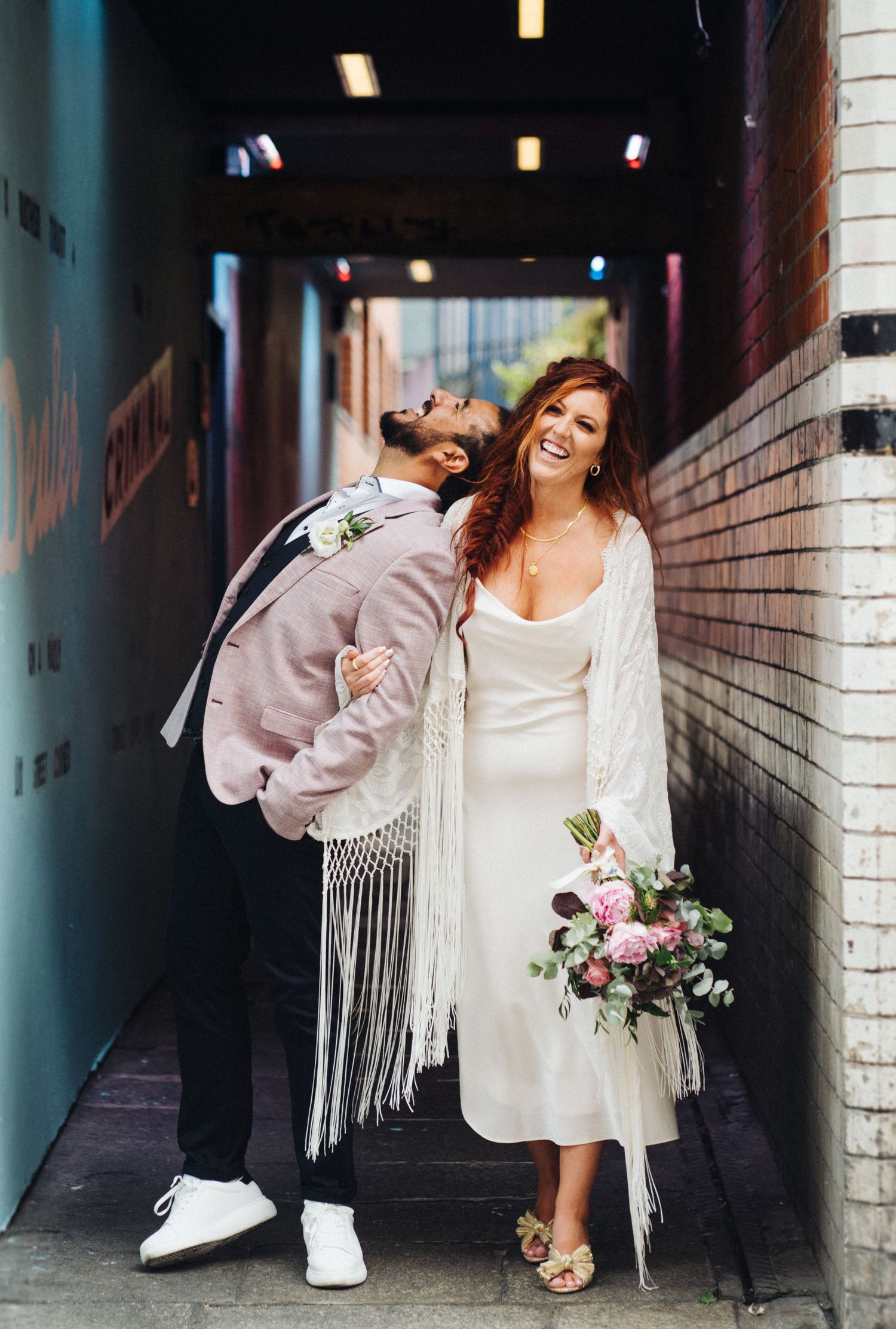 Candid wedding portrait of a couple laughing together in an urban alleyway.