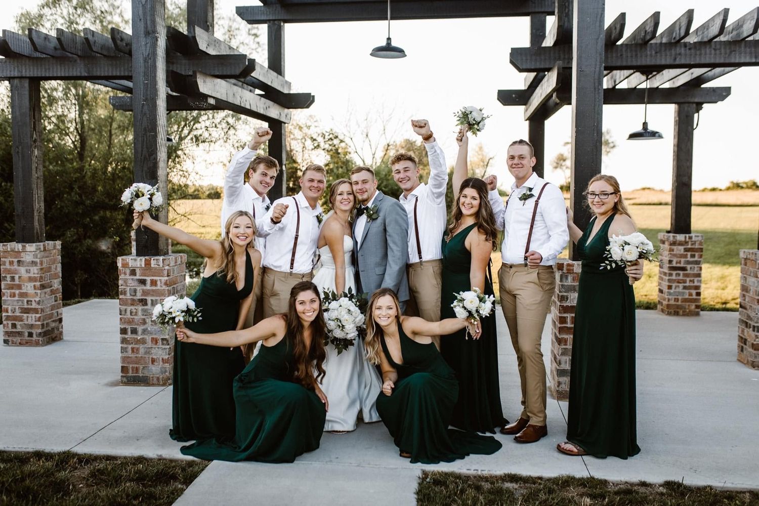 Wedding party gathered under outdoor pergola with brick pillars.
