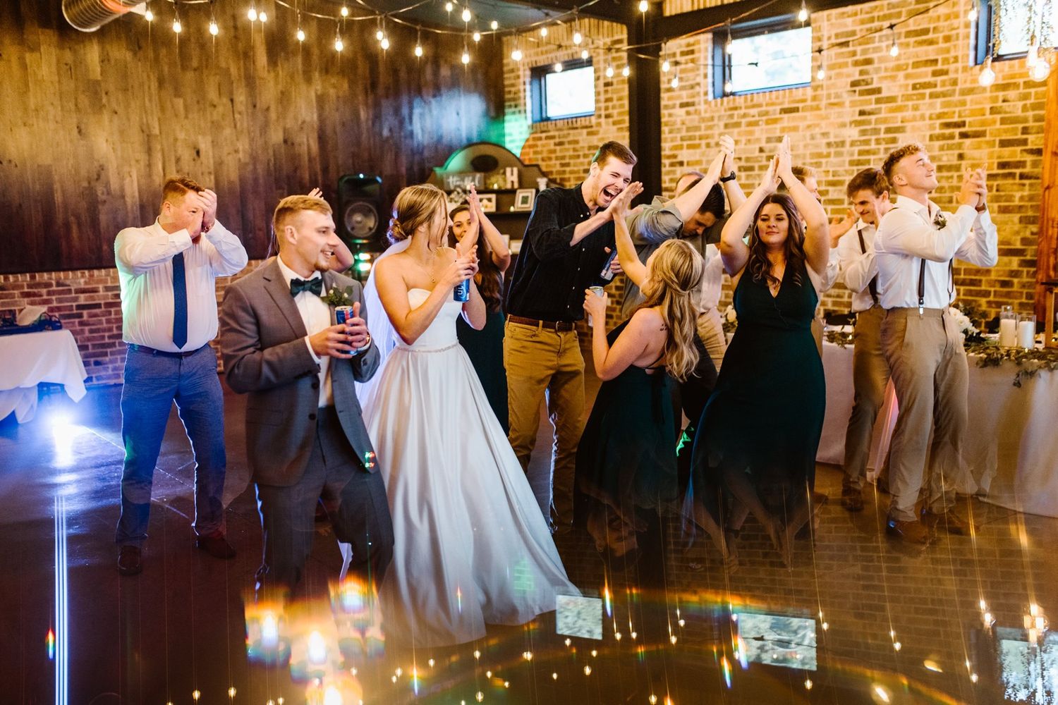 Wedding celebration on dance floor with string lights and brick walls creating festive atmosphere.