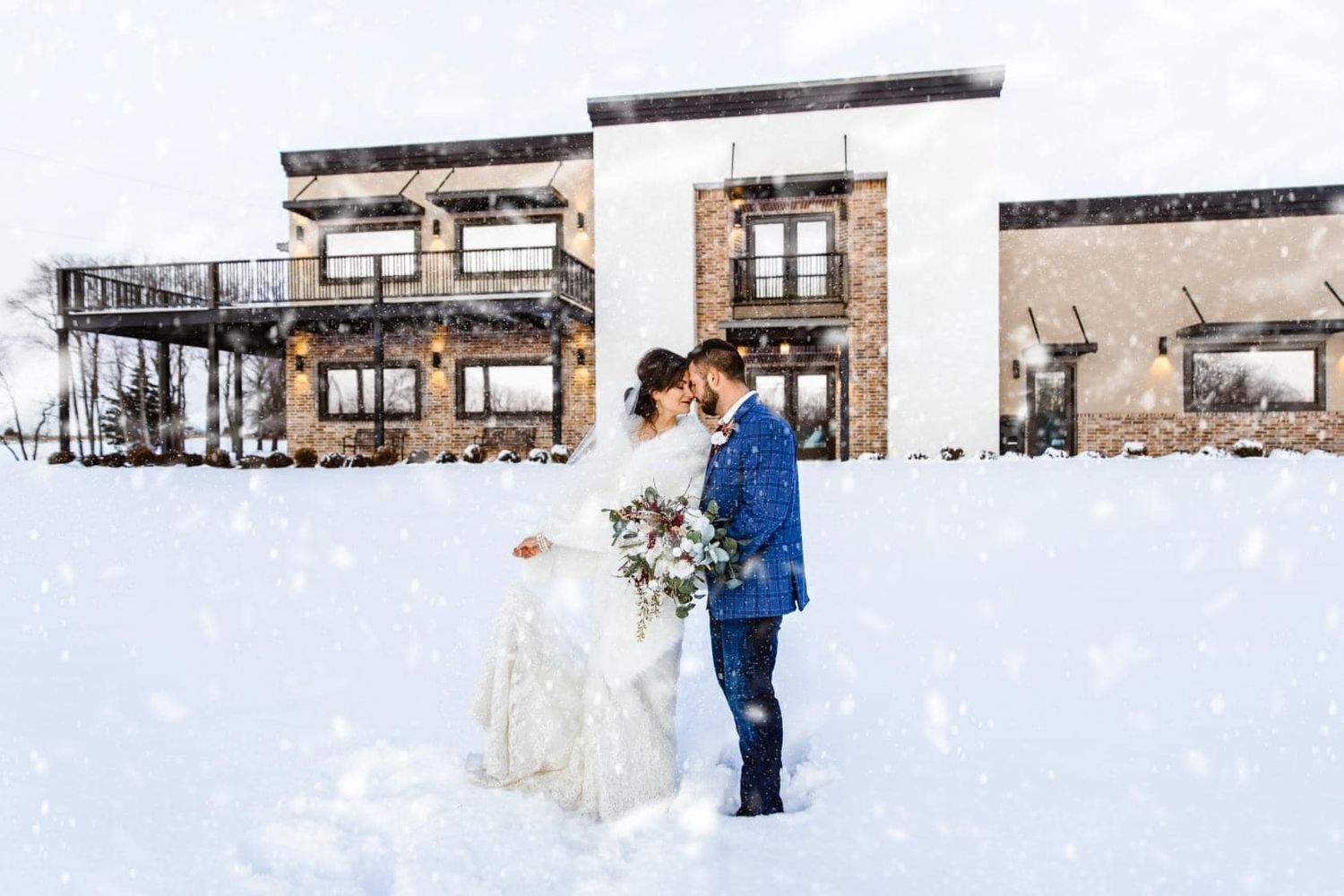 Winter wedding portrait in front of modern building surrounded by snow.