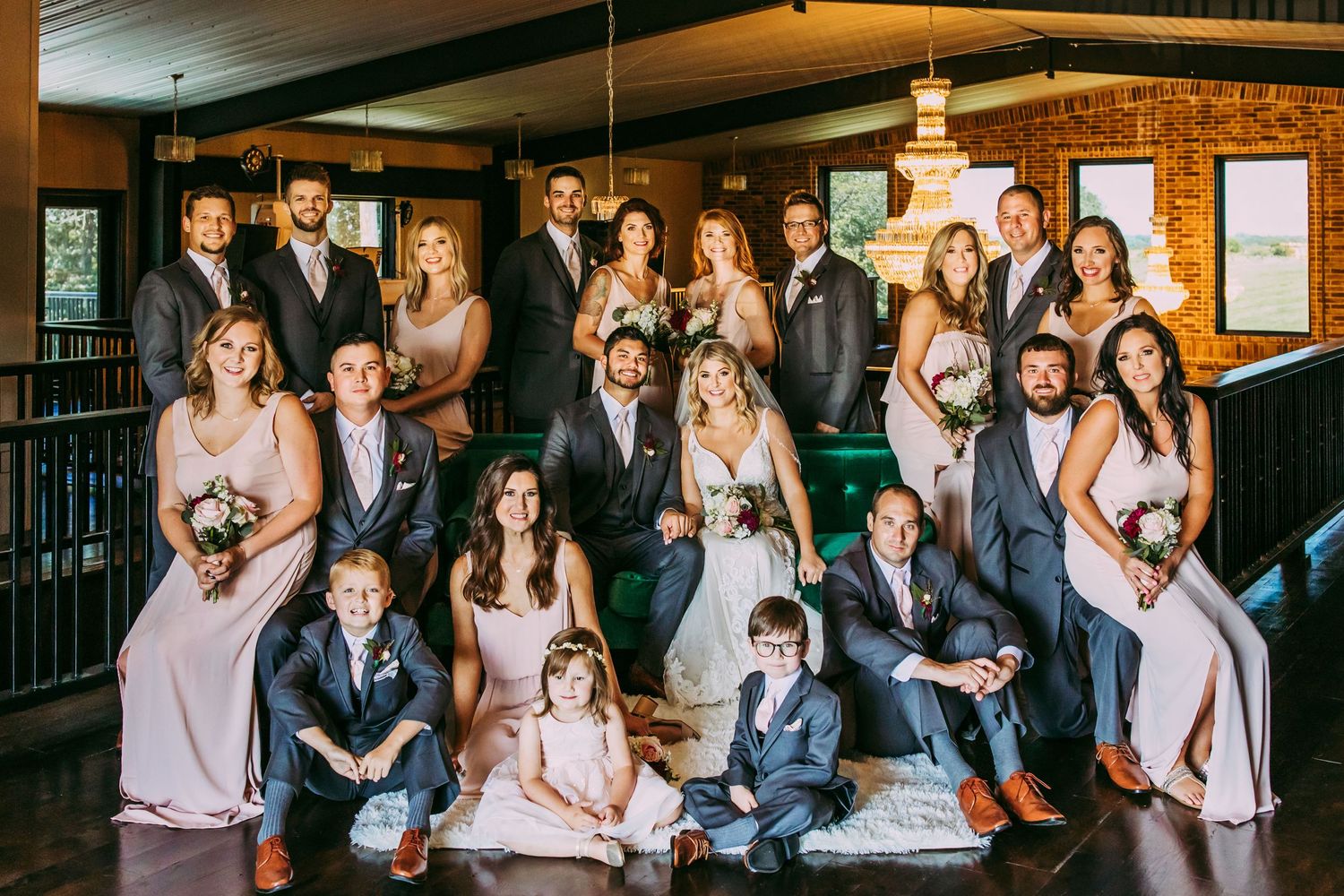 Wedding party in formal attire poses together in an elegant indoor venue with dark wood and warm lighting.