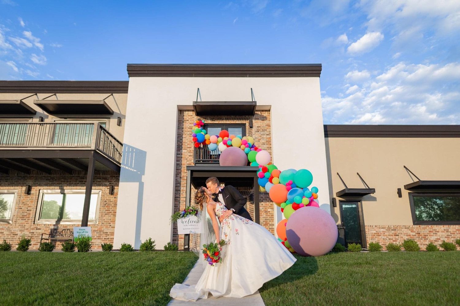 Celebratory wedding scene with colorful balloons against modern building exterior.