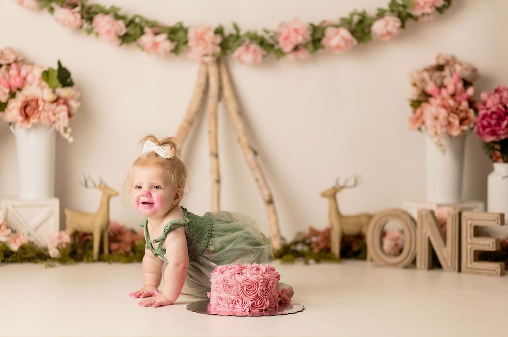 Baby in green outfit with pink floral garland and ONE sign for cake smash photo.