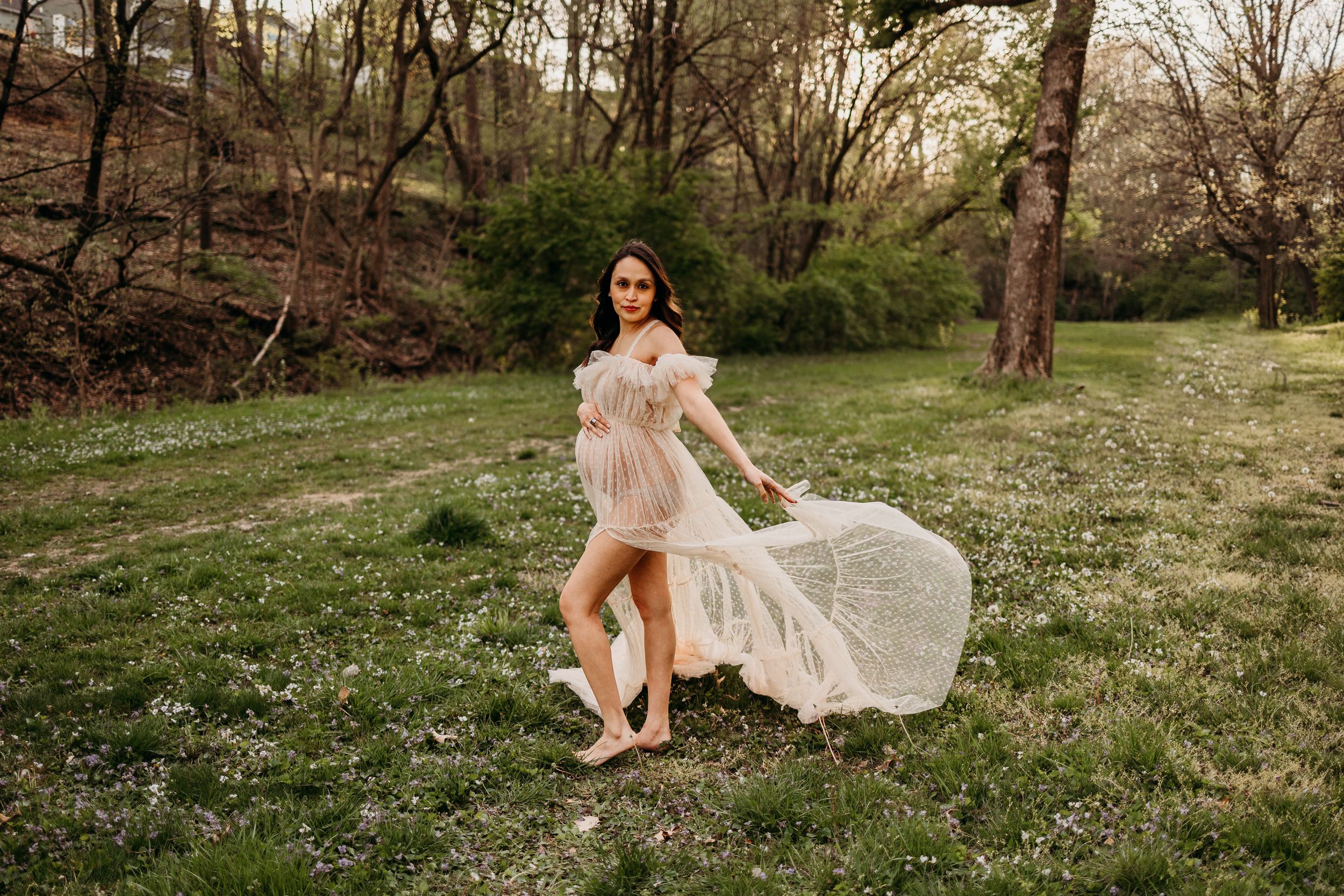 A flowing blush gown billows in the breeze during an outdoor spring photoshoot in a grassy meadow.