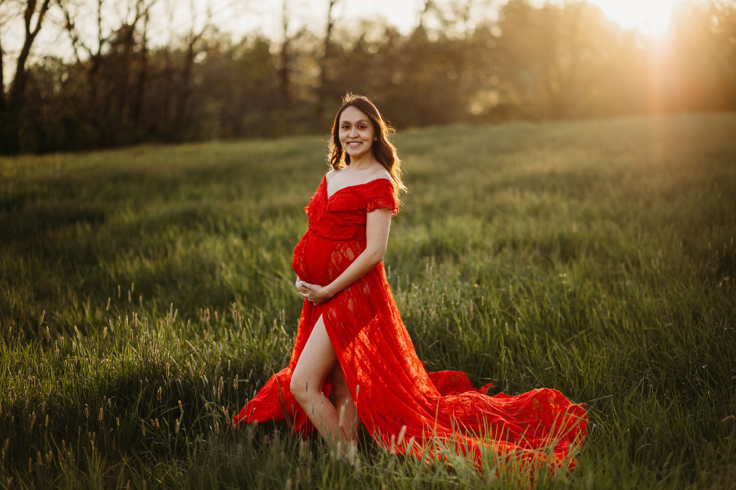 A flowing red dress catches the sunlight in a grassy field during golden hour.