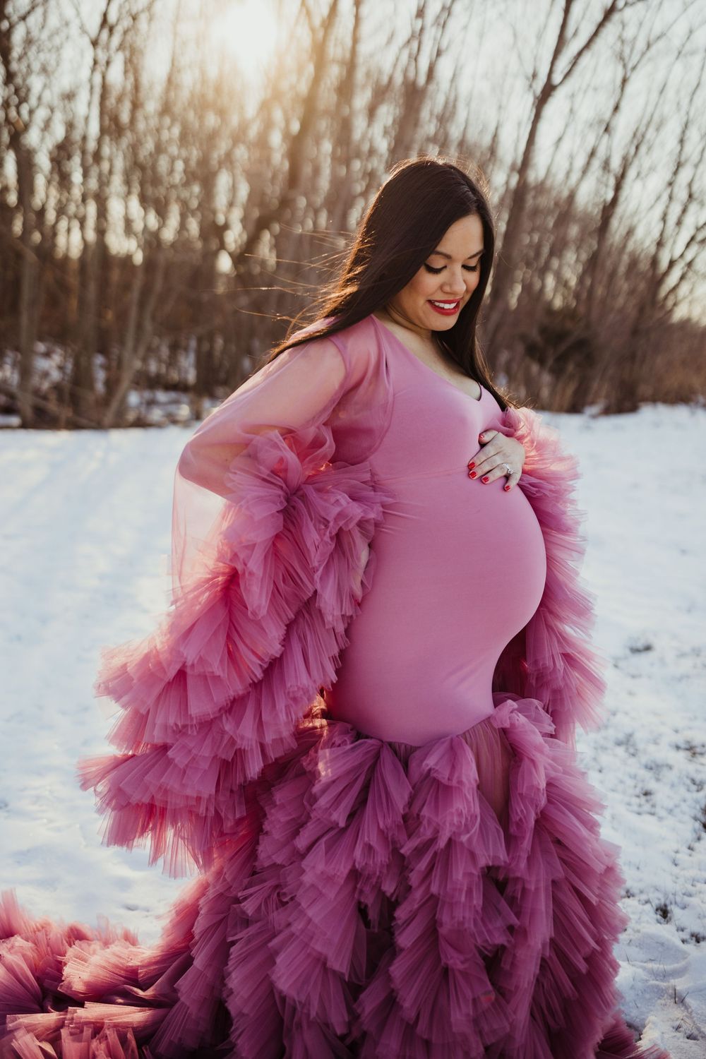 A stunning ombre tulle maternity gown in shades of pink and purple photographed against a snowy winter landscape.