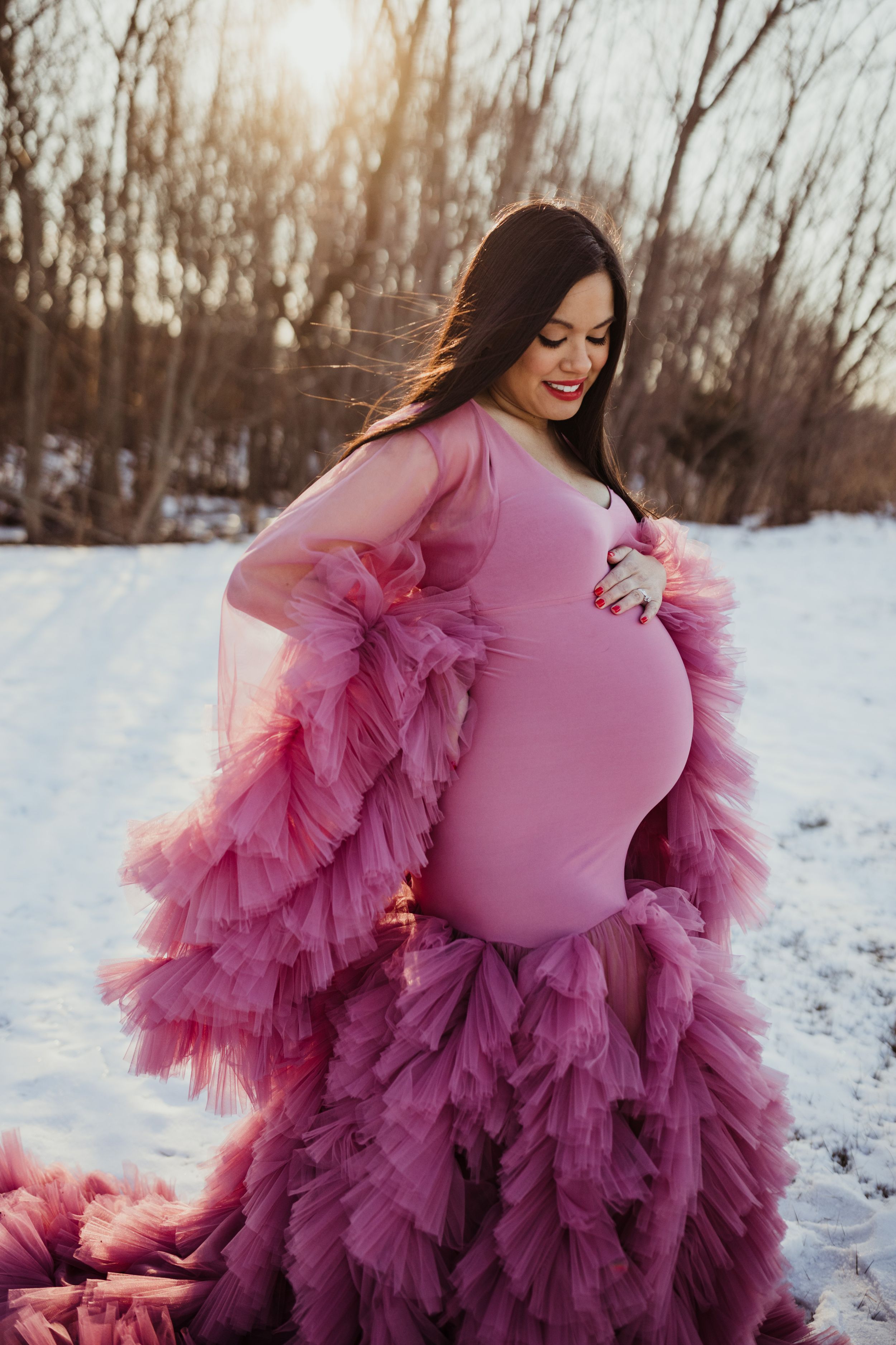 A stunning ombre tulle maternity gown in shades of pink and purple photographed against a snowy winter landscape.