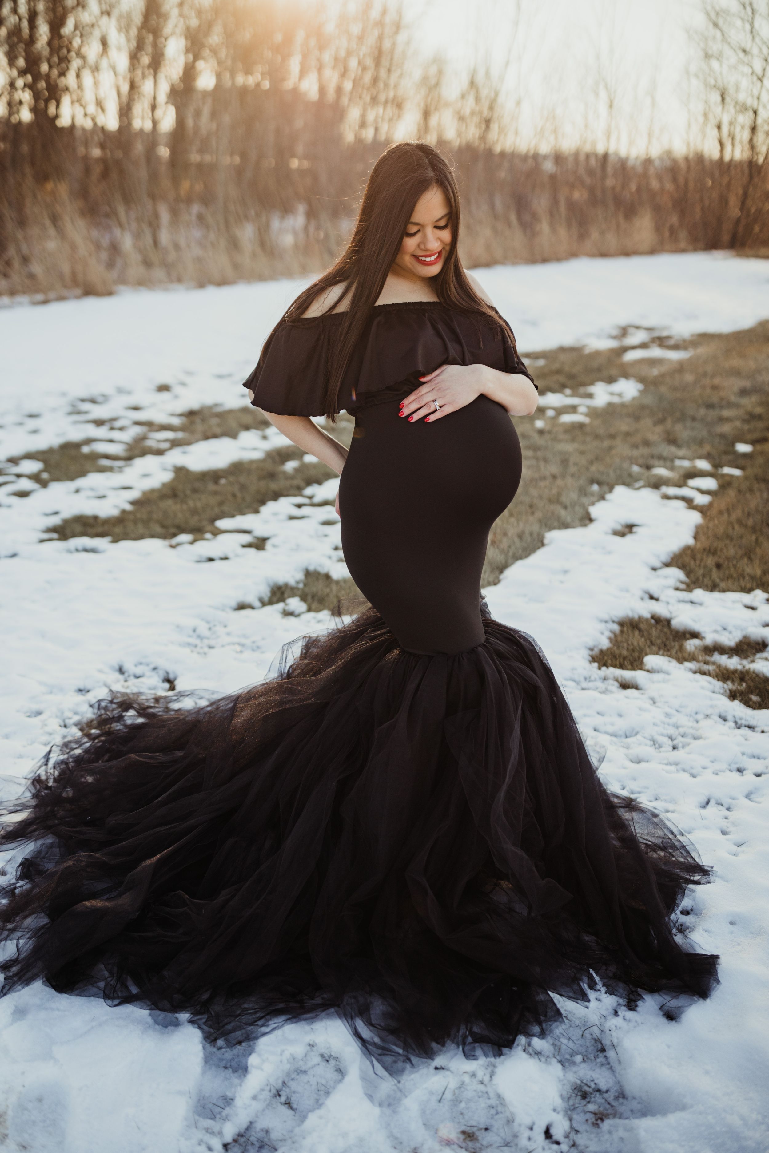 Dramatic black tulle maternity gown photographed in snowy winter landscape at sunset.