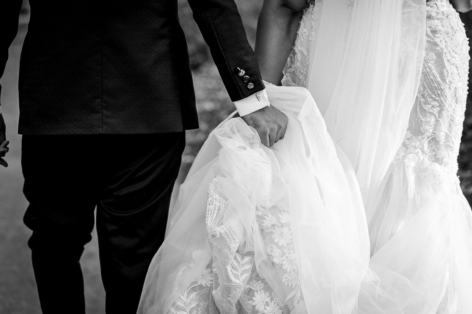 Black and white detail shot of wedding dress lace and groom's tuxedo.