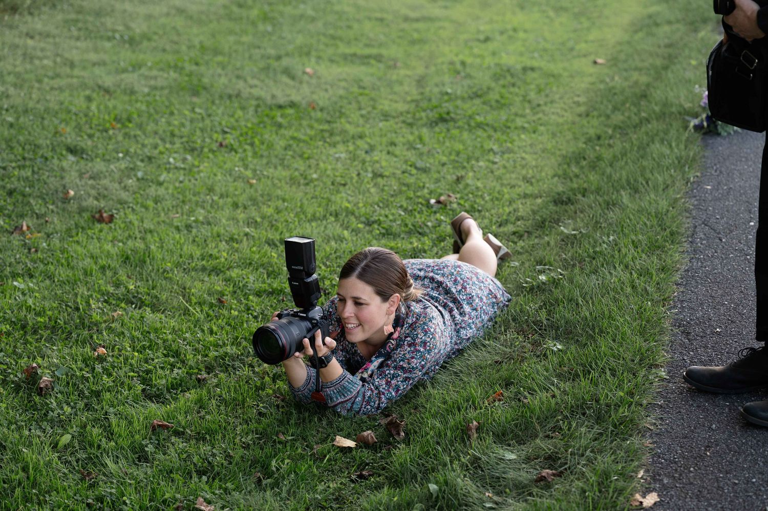 Wedding photographer lying on grass to capture the perfect shot with professional camera.