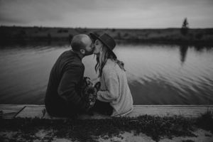 A romantic black and white photo of a couple sharing a tender moment on a dock by a tranquil lake.