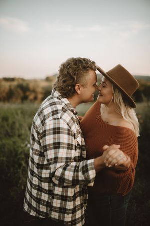 A romantic couple embraces in a field during golden hour while sharing an intimate moment.
