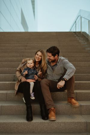 A family sits together on concrete steps sharing a tender moment.