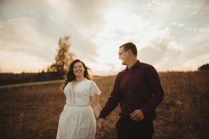 Couple walking hand in hand through a field during golden hour engagement session.