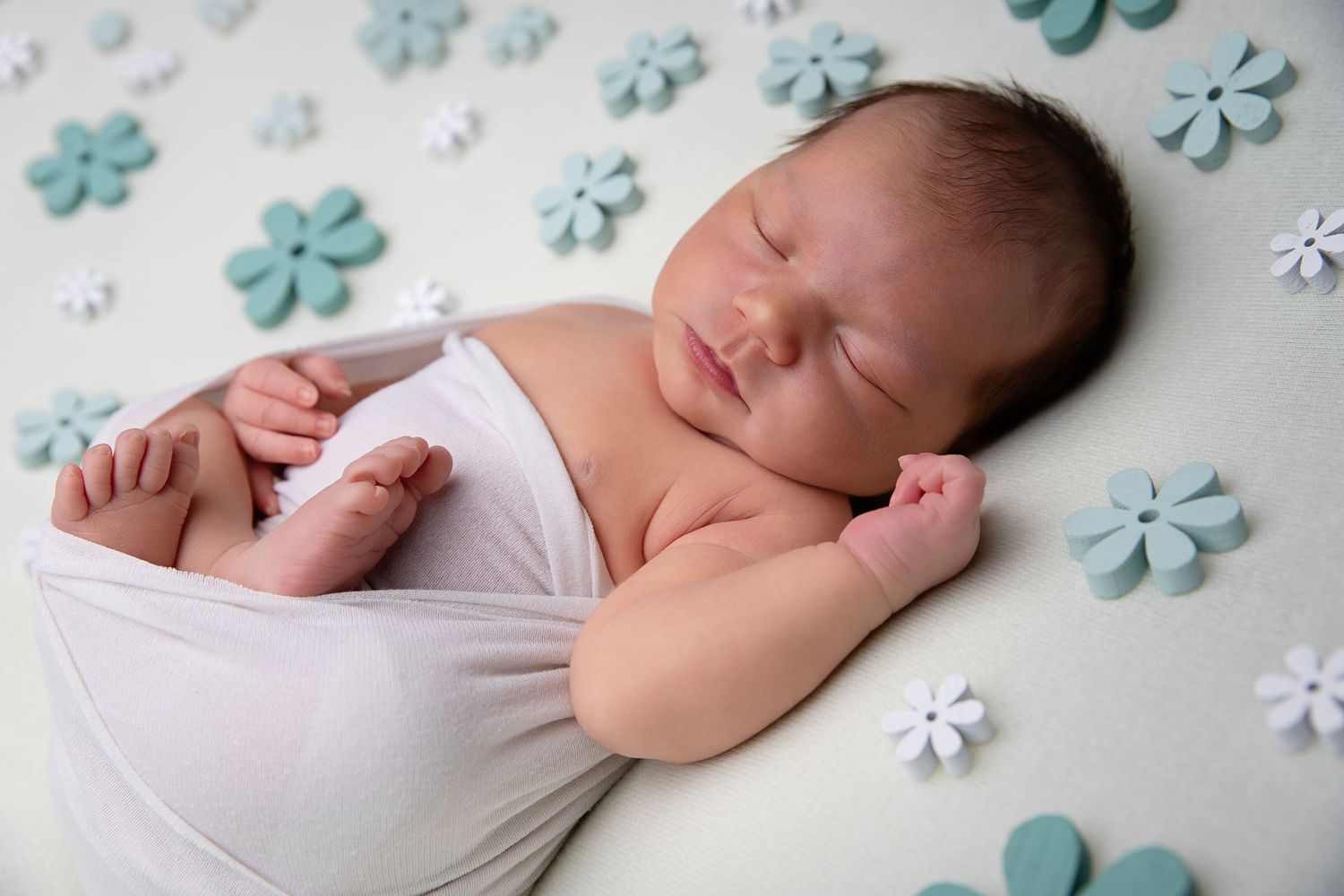 Peaceful sleeping newborn surrounded by blue paper flowers on white fabric.