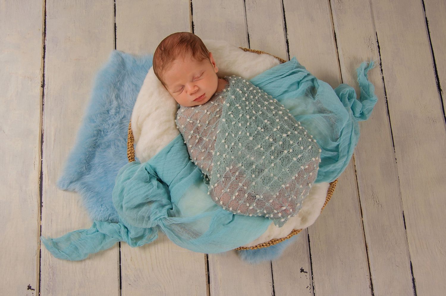 newborn photography of baby boy sleeping in fluffy basket with baby blue colours wrapped around him