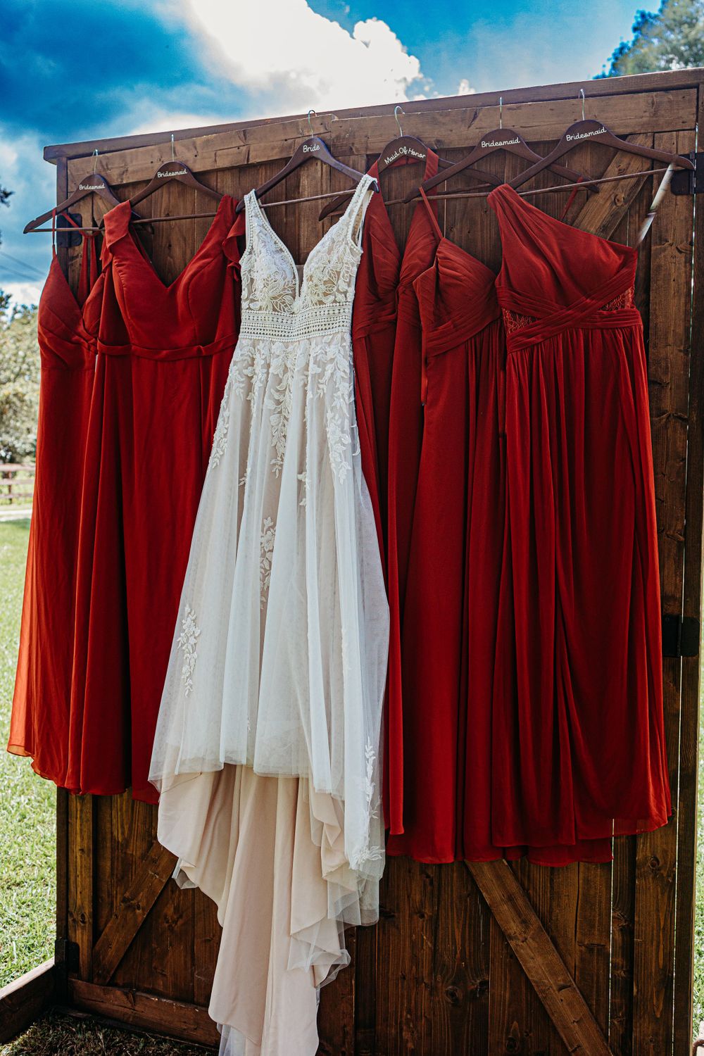 Wedding party dresses displayed on wooden backdrop with white bridal gown flanked by red bridesmaid dresses.