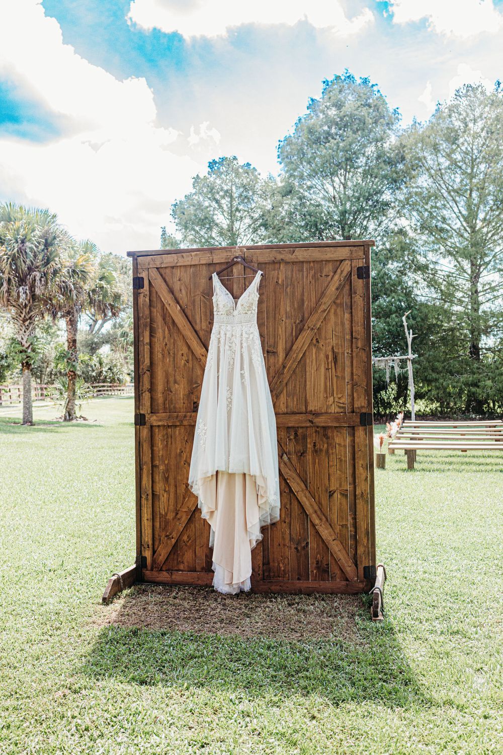 White wedding dress hanging on rustic wooden barn doors in an outdoor garden setting.