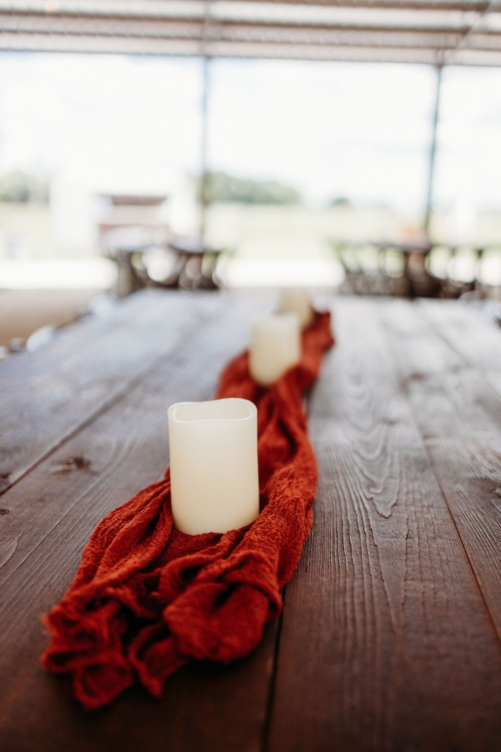 White pillar candle on red fabric runner across rustic wooden table.