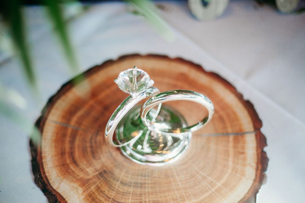 Wedding rings displayed on rustic wood slice with diamond solitaire engagement ring.
