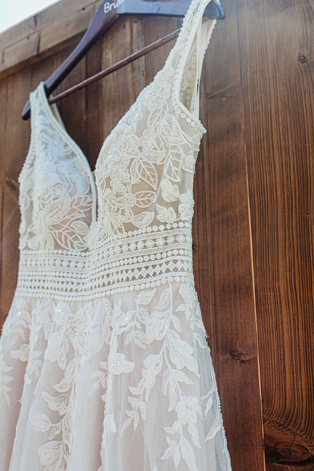 Close-up of lace detail on a white wedding dress bodice hanging against wooden background.