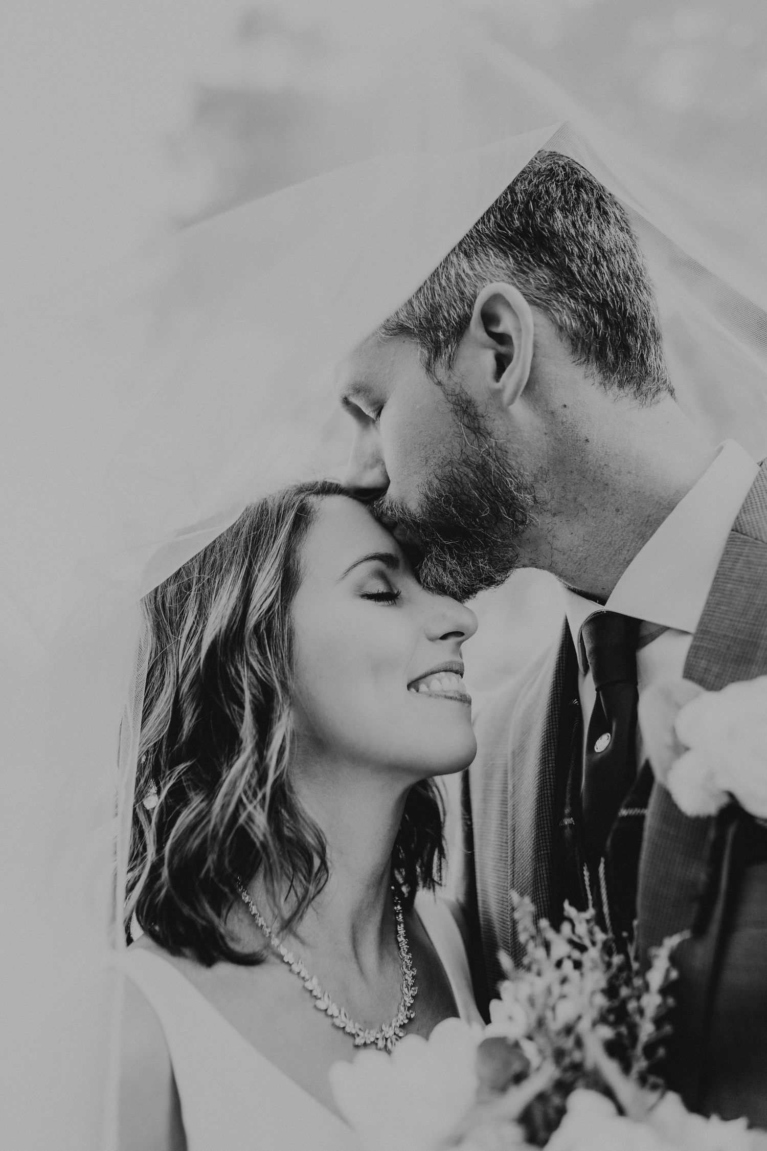 Groom kisses bride on the forehead under her veil